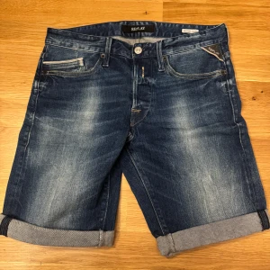 Blå jeansshorts från Replay - Säljer ett par snygga blå jeansshorts från Replay i mycket bra skick. De har en klassisk femficksdesign med knappar och dragkedja. Perfekta för sommaren med en avslappnad stil och uppvikta ben. Passar både till vardags och lite mer dressade tillfällen.