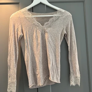 Beige långärmad topp med spetsdetaljer från Intimissimi - Använt tröjan 1-2 gånger o köpte den för nån vecka sedan men är inte min stil. Så Säljer en superfin beige långärmad topp från Intimissimi. Den har vackra spetsdetaljer vid halsringningen och ärmsluten som ger en romantisk touch. Perfekt för både vardag och fest! 💫