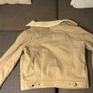 Beige jacka med foder - Säljer en snygg beige jacka med mjukt foder. Den har en klassisk design med knappar framtill och två bröstfickor. Perfekt för höst och vår när det är lite kyligt ute. Jackan har långa ärmar och en skön krage. Orginalpris 899kr!