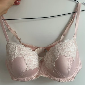 Rosa bh från Fifty Shades of Grey - Säljer en elegant rosa bh från Kappahl collecotion -Fifty Shades of Grey. Den har vackra spetsdetaljer i vitt och är gjord i ett glansigt satinmaterial. Bh:n har justerbara axelband och en liten öppning framtill för en extra touch av stil. 