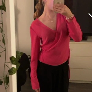 Rosa omlottopp från Monki - Säljer en superfin rosa omlottopp från Monki i storlek XS. Toppen har långa ärmar och en snygg omlottdesign som ger en smickrande passform. Perfekt för både vardag och fest!