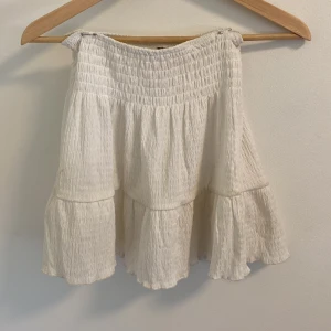 Vit volangkjol - Säljer en superfin vit kjol med volanger. Den är gjord i ett lätt och luftigt material, perfekt för sommardagar. Kjolen har en elastisk midja som gör den bekväm att bära. Den har en superliten fläck men som jag aldig lagt märke till de få gånger jag har använt den! Älskar den men har tyvärr blivit för liten och kommer inte till användning!