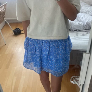 Blå blommig kjol från Pieces - Säljer en superfin blå kjol från Pieces i storlek S. Den har ett sött blommigt mönster och en bekväm elastisk midja. Kjolen är perfekt för sommardagar. Den har volanger som ger en extra touch av stil. använt 1 gång💕