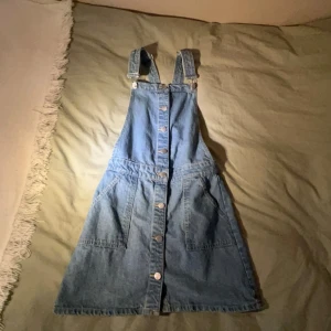 Jeansklänning med knappar - Säljer en superfin jeansklänning med knappar framtill. Den har justerbara axelband och stora fickor på sidorna. Perfekt för en avslappnad look! 💙