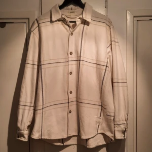 Vit och svart rutig skjorta från Pull&Bear - Säljer en snygg vit skjorta från Pull&Bear med ett stilrent svart rutmönster. Skjortan har långa ärmar och knappar framtill. Perfekt för både vardag och fest! 🖤