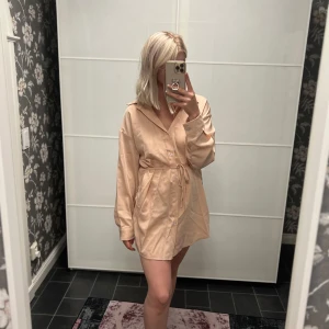 Champagnefärgad kortklänning med knytband - Säljer en elegant champagnefärgad kortklänning med knytband i midjan som även har shorts. Klänningen har långa ärmar och en stilren design som passar perfekt för festliga tillfällen. Materialet ser ut att vara mjukt och bekvämt, vilket gör den både snygg och skön att bära. har även en turkos i samma modell om nån är sugen på det