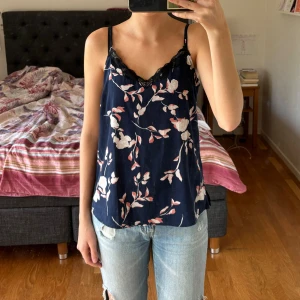 Mönstrad Spetslinne - Mönstrad topp med spetskant upptill. Mörkblå med rosa/vita blommor. Från Vero Moda i storlek M.