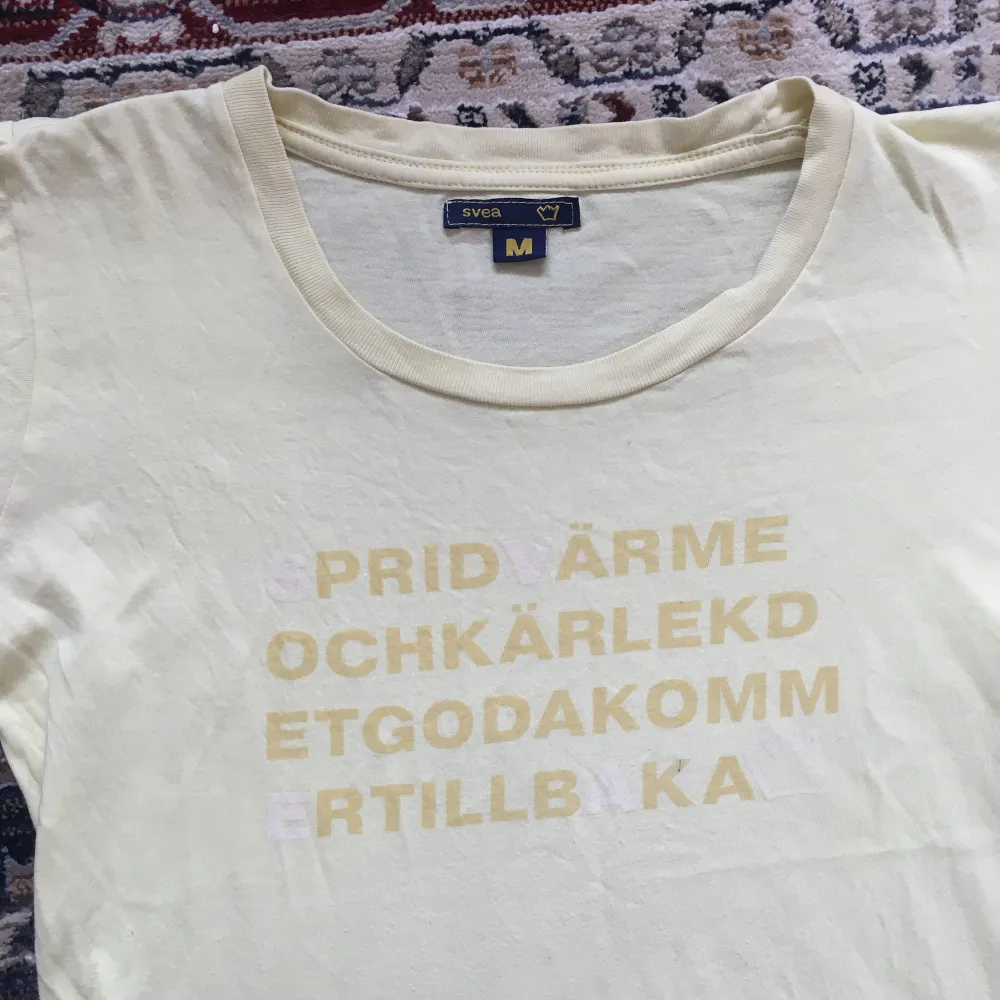 Ljusgul T-shirt med vit/gul text på från Svea där det står, ”sprid värme och kärlek och det goda kommer tillbaka”. T-shirts.