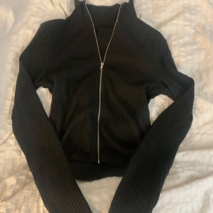 Svart ribbad tröja med dragkedja - Säljer en svart ribbad tröja med dragkedja framtill. Den är långärmad och perfekt för både höst och vinter. Tröjan är stilren och passar till det mesta. Perfekt för en casual look eller att klä upp med accessoarer.