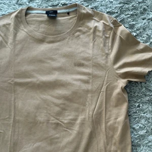 Beige t-shirt från BOSS - Säljer en snygg beige t-shirt från BOSS i storlek S. Den är i slim fit och perfekt för en stilren look. T-shirten är gjord av mjuk bomull, använd 1 gång 