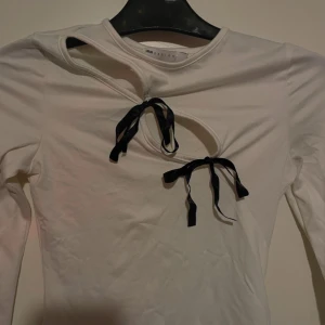 Vit långärmad topp från ASOS DESIGN - Säljer en superfin vit långärmad topp från ASOS DESIGN. Den har en unik design med två svarta knytband framtill som ger en cool detalj. Perfekt för både vardag och fest! ✨