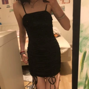 Svart klänning - Säljer en superfin svart klänning. Klänningen har en snygg rynkad detalj med knytning framtill som ger en extra touch och man kan ändra längden på den genom den. Passar perfekt för en utekväll eller nyårsfesten. jag är 170cm
