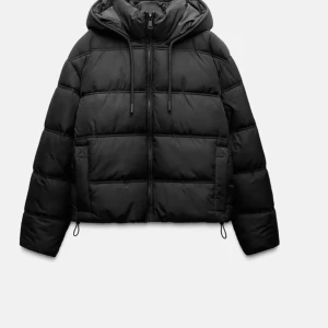 Svart pufferjacka med huva - Säljer en snygg och varm svart pufferjacka med huva. Jackan har dragkedja framtill och är perfekt för kalla dagar. Den är både stilren och praktisk med sin vadderade design.