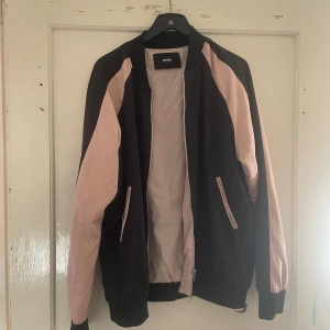 Svart och rosa bomberjacka från Bik Bok - Säljer en snygg bomberjacka från Bik Bok i svart och rosa med en cool drake broderad på ryggen. Jackan har dragkedja och långa ärmar, perfekt för höst och vår. Den är i bra skick och passar både till vardags och fest.