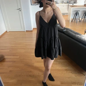 Svart kortklänning med volangdetaljer - Säljer en superfin svart kortklänning med smala axelband och volangdetaljer. Perfekt för sommardagar eller en festkväll. Klänningen har en luftig passform och är riktigt bekväm att bära. Passar perfekt med ett par snygga klackar