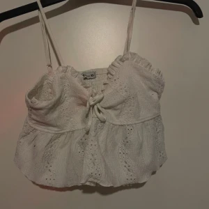 Vit spetslinne från Sister KS - Säljer ett supersött vitt spetslinne från Sister KS i storlek XS. Linnet har smala axelband och en fin knytdetalj framtill. Perfekt för sommardagar eller en festlig kväll. Det är i nyskick och redo för nya äventyr! 🌸