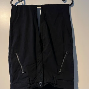 Svarta byxor med dragkedjor - Säljer ett par svarta byxor i bra skick. De har coola dragkedjor på sidorna och en knapp framtill. Perfekta för en casual look eller en utekväll. Passar till det mesta och är superbekväma!