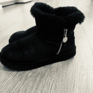 Svarta boots från UGG - Säljer ett par svarta UGG-boots i mocka med mjukt foder. De har en dragkedja på sidan för enkel på- och avtagning. Perfekta för kalla dagar när du vill hålla fötterna varma och bekväma. Använt skick fortfarande fina!