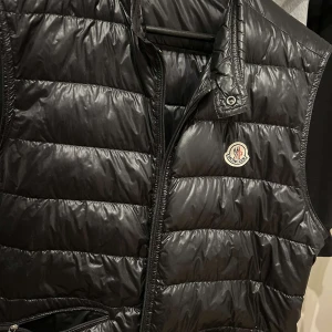 Moncler väst - Säljer en moncler väst i otroligt bra skick, äkta såklart Storlek M ✅ Västen har en glansig finish och är perfekt för kommande dagar. Passar både till vardags och lite finare tillfällen. Perfekt för höst, vinter och våren 🙏🏾