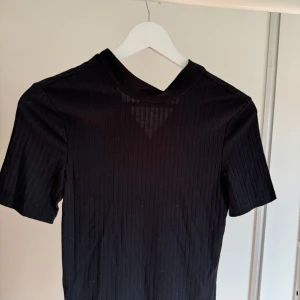 Svart t-shirt - T-shirten är i ribbat material. Den är svart med en liten polokrage. Tröjan är i storlek xs. 