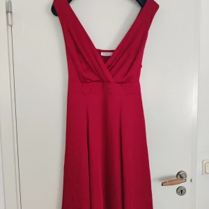 Festlig klänning  - En vinröd festlig klänning. Har dragkedja på sidan och band att knyta samt dubbel tyg så den är inte genomskinlig. Finns en dov fläck framtill och små små hål efter  att ha haft en säkerhetsnål där. Se bilder. 