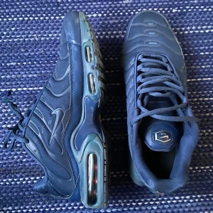 Blå Nike TN Sneakers  - Säljer ett par snygga blå Nike sneakers i bra skick. De har en cool design med synliga luftkuddar i sulan och klassisk snörning. Perfekta för både vardag och träning!