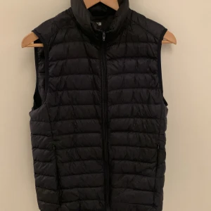 Svart dunväst från Uniqlo - Säljer en stilren svart dunväst från Uniqlo i storlek XS. Västen har en dragkedja framtill och är lättviktig med vattenavvisande material. Perfekt för lager-på-lager under kyliga dagar.