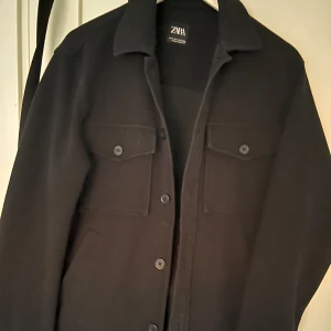 Svart jacka från Zara - Snygg svart jacka från Zara med knappar framtill och två bröstfickor. Perfekt för en stilren look.
