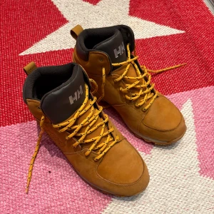 Bruna boots från Helly Hansen - Snygga bruna boots från Helly Hansen i premiumläder med robust sula och snörning. Perfekta för höst och vinter med en stilren design och bekväm passform.