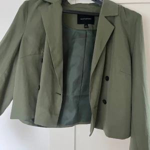 Olivgrön kavaj från Banana Republic - Snygg olivgrön kavaj från Banana Republic med klassisk design och knappar framtill. Perfekt för en stilren look. Passar både till vardags och mer formella tillfällen. Stl 12 typ som S