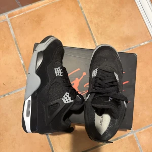 Svarta Nike Air Jordans - Säljer ett par svarta Nike Air Jordans med grå och vita detaljer. Skorna har en klassisk design med snörning och en synlig luftdämpning i sulan. Perfekta för sneaker-entusiaster!