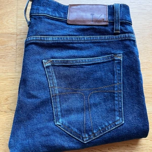 Blå jeans från tiger of sweden - Snygga blå jeansbyxor från tiger of sweden med klassisk femficksdesign. Tillverkade i Italien, dessa jeans har en slim/straigth passform och midwaist. Perfekta för en stilren look.