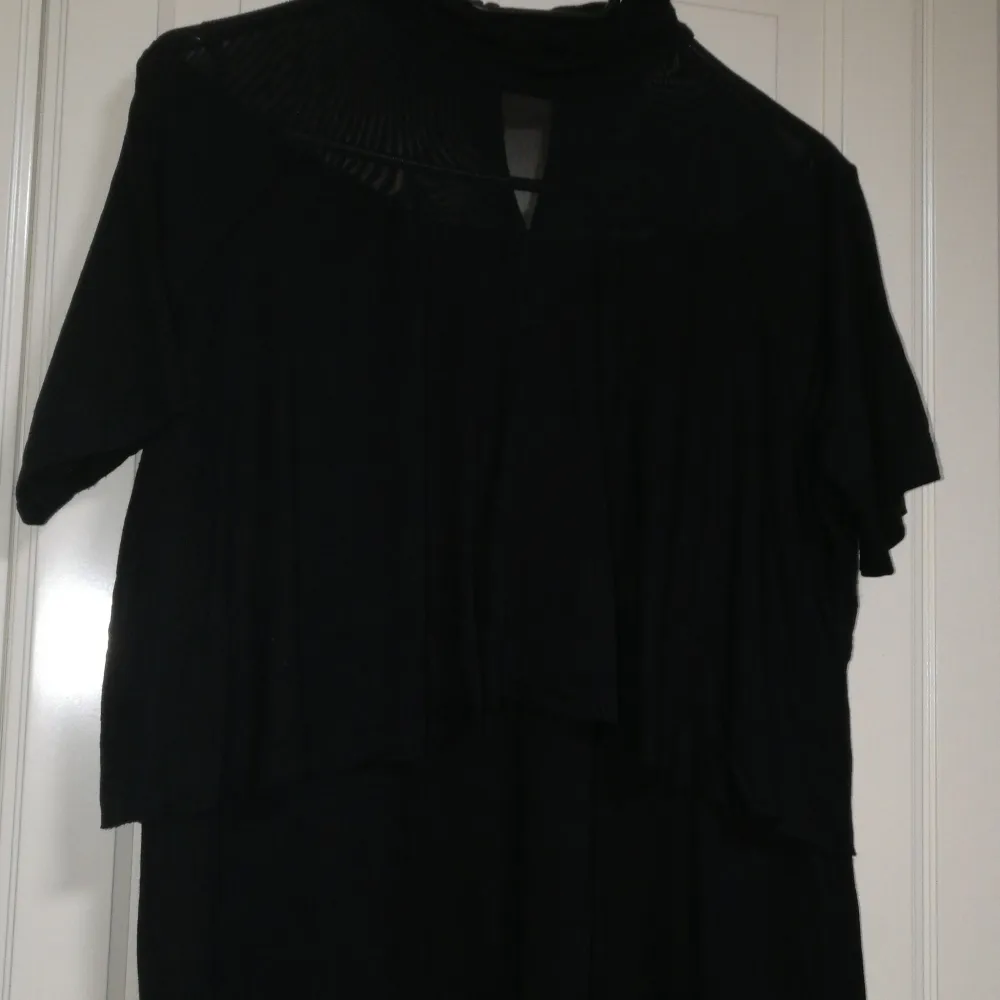Elegant svart klänning från ASOS med korta ärmar och hög krage. Perfekt för en stilren look. Klänningen har en diskret design som passar många tillfällen, mesh detaljer innan den högre veckade kragen. . Mekot.