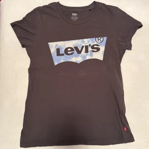 Svart t-shirt från Levi's - Mycket använd med skönt material. Snygg svart t-shirt från Levi's med ett stort logotryck i blått och vitt på framsidan. Perfekt för en casual look. Tillverkad i mjukt bomullsmaterial för extra komfort.