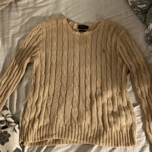 Beige stickad tröja från Ralph Lauren - Säljer en beige stickad tröja från Ralph Lauren i Pima Cotton. Nypriset är 2700. Tröjan har ett kabelstickat mönster och en diskret logga på bröstet. Storlek L men skulle säga att den är mer som M! Använd typ 1 gång!
