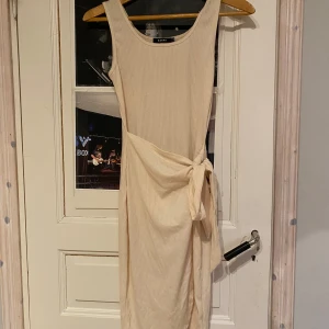 Beige ribbad klänning  - Snygg beige ribbad klänning med knytning i midjan. Den är ärmlös och har en stilren design som passar perfekt för varmare dagar.