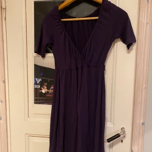 Mörklila omlottklänning - Snygg mörklila omlottklänning med v-ringning och korta ärmar. Perfekt för en stilren look.