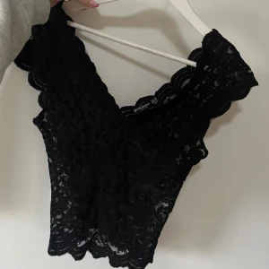 Svart spetslinne från Stradivarius - Säljer ett elegant svart spetslinne från Stradivarius. Linnet har en v-ringad design med vackra spetsdetaljer och är perfekt för en stilren look. Passar utmärkt till både vardag och festliga tillfällen.