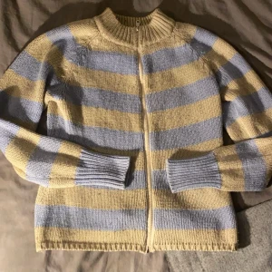 Randig stickad kofta med dragkedja - Mysig stickad kofta i ljusblått och beige med dragkedja framtill. Den har långa ärmar och ribbade muddar vid ärmslut och nederkant. Perfekt för kyliga dagar!