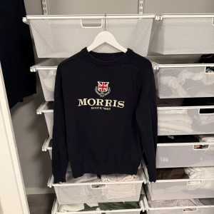 Mörkblå tröja från Morris - Snygg mörkblå tröja från Morris med broderad logga och text framtill. Tröjan har långa ärmar med siffran 68 på ena ärmen. Perfekt för en stilren look. Storlek L