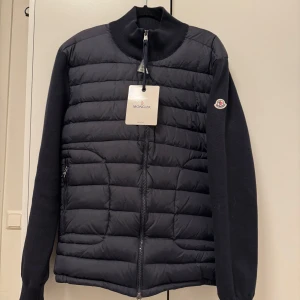 Moncler cardigan passar L/M  - Snygg svart pufferjacka från Moncler med dragkedja och långärmad design storlek XL men passar L och M. Jackan har en quiltad stil och Moncler-logga på ärmen. Perfekt för hösten och våren. Jackan är helt ny oanvänt och i bra skick utan skador. NFC funkar och allt. Pris 1599och kan diskuterats vid snabb affär.