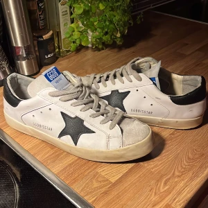 Golden Goose intressekoll - Snygga Golden Goose Superstar sneakers i vitt med svarta detaljer och stjärna på sidan. Det kommer ej med låda. Öppen för byten. Det finns defekter på sulan då den har lotsnad lite men det går att fixa