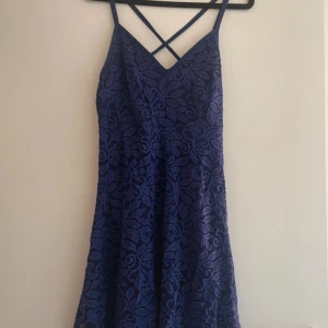 Blå spetsklänning från Body Flirt - Snygg blå klänning i spets från Body Flirt med smala axelband och korsad rygg. Perfekt för en somrig look med sin blommiga spetsdesign. Klänningen har en figurnära passform upptill och faller fint nedtill.