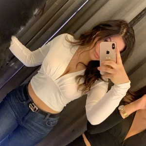 Vit topp - Snygg vit omlottopp med v-ringning och långa ärmar. Toppen är croppad och har en stilren design som passar perfekt till både jeans och kjol. Använd en gång