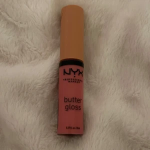 NYX Butter Gloss - Säljer ett NYX Butter Gloss i en härlig rosa nyans. Perfekt för att ge läpparna en mjuk och glansig finish. Kompakt och lätt att ta med sig i väskan.