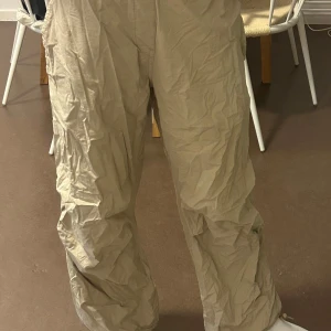 Beige cargobyxor - Säljer ett par beige cargobyxor/parachute pants med flera fickor och en loose passform. Perfekta för en avslappnad stil. Byxorna har en klassisk design med praktiska detaljer.
