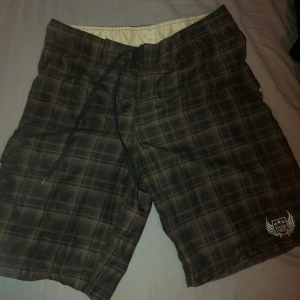 Bruna rutiga shorts från Billabong - Säljer ett par bruna rutiga shorts från Billabong med snörning i midjan och coola detaljer. 