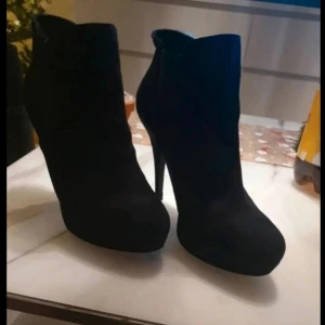 Svarta stövletter med klack - Snygga svarta stövletter med hög klack och spetsig tå, mocka imitation. Perfekta för en elegant look. Klackarna har inte kommit till användning på ca 2 år. Fortfarande i fint skick, det är på sulan man ser att de är använda( vilket kan ses på sista bilden) Storlek: 39 Klackhöjd: 10,5 Platåhöjd: 2cm