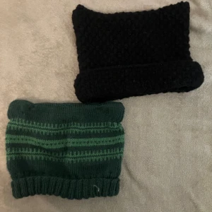 Två stickade mössor i svart och grönt - Säljer två mysiga stickade mössor med katt öron. Den ena är svart och är köpt och den andra är grön med ränder och är egen stickad. Perfekta för kalla dagar. Säljer 30 kr styck eller 50 för båda.