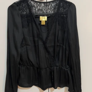 Svart blus med spetsdetaljer - Elegant svart blus från H&M med spetsdetaljer vid axlar och rygg